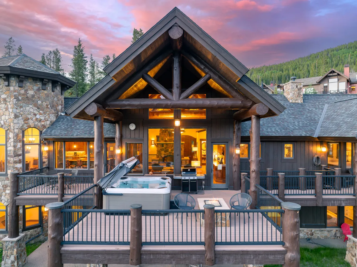 An inviting exterior shot of a luxurious hot tub on a deck, surrounded by stone architecture and large windows. The setting overlooks a stunning mountain landscape, blending comfort and relaxation with scenic views.
