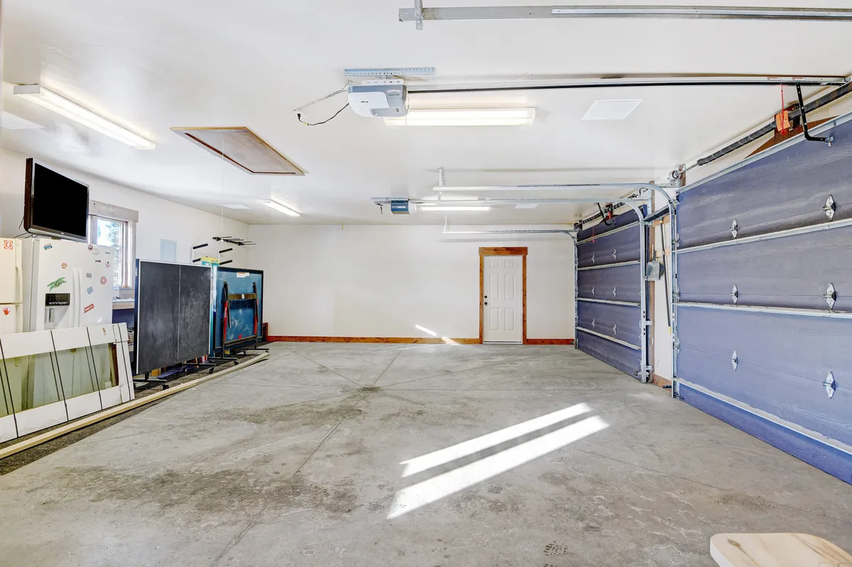 A spacious garage area featuring garage doors, a workbench, storage cabinets, and a TV. The open, practical layout is ideal for organizing ski gear or prepping for mountain adventures.