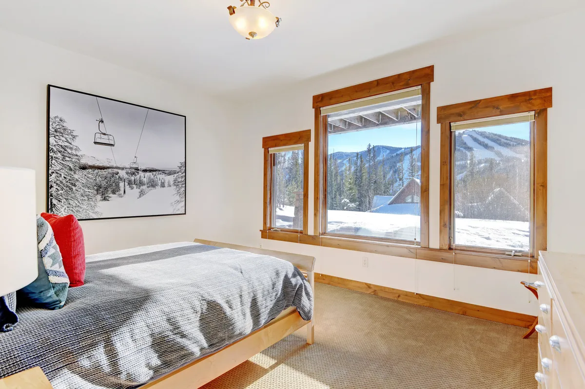 A serene guest bedroom with a comfortable bed dressed in soft patterned linens, large windows that frame spectacular mountain views, and tasteful decor. The space feels peaceful and inviting, ideal for restful sleep and privacy.