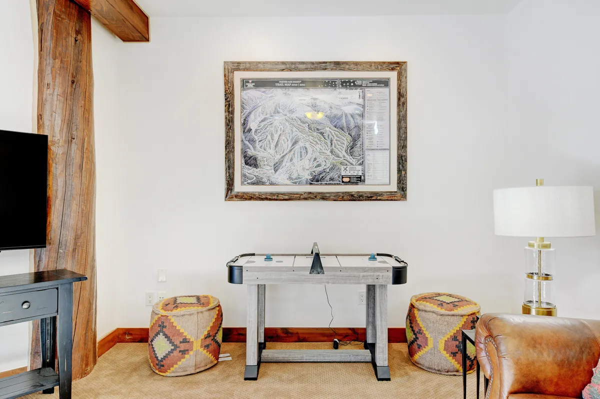 A lively game room featuring an air hockey table as the focal point, complemented by colorful stools, a framed map on the wall, and soft ambient lighting. The space exudes a playful atmosphere, perfect for friendly competitions and group bonding.