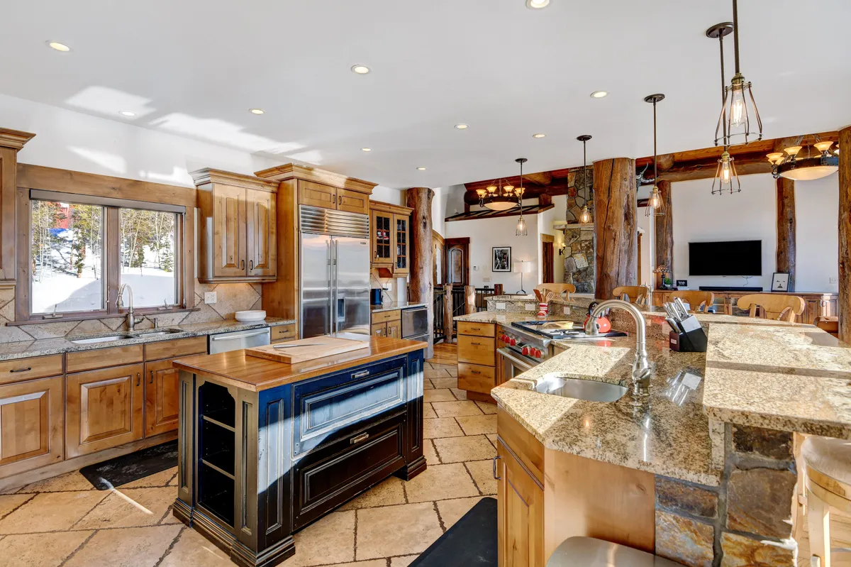 A large kitchen with a central island, gleaming stainless steel appliances, granite countertops, rich wood cabinetry, and generous windows letting in natural light. The room is designed for cooking, entertaining, and family gatherings, exuding a sense of warmth and hospitality.